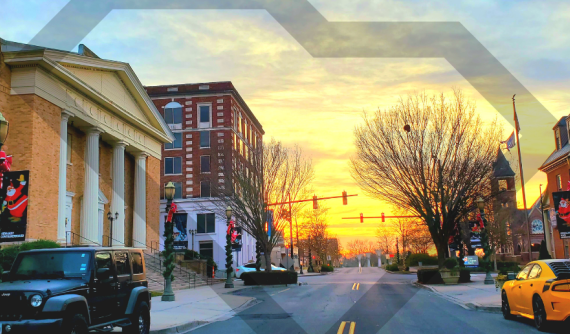 View of street in Rock Hill, SC at sunset with a jeep parked on the side of the road and several building in sight.